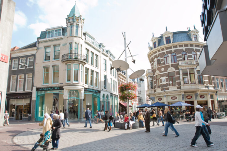 Belebter Platz mit Menschen vor dem Musiskwartier-Gebäude in Arnheim, das eine weiße Fassade und grüne Fensterrahmen hat.