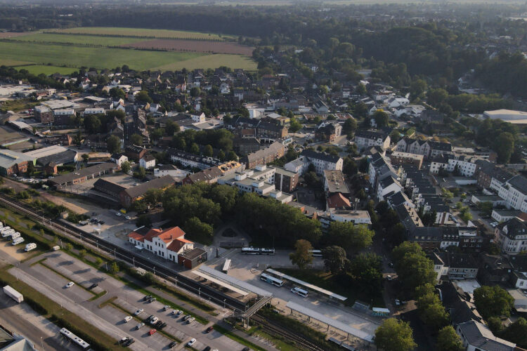Luftaufnahme von Kleve mit Bahnhof, Parkplätzen, Wohnhäusern und Feldern im Hintergrund bei Tageslicht.