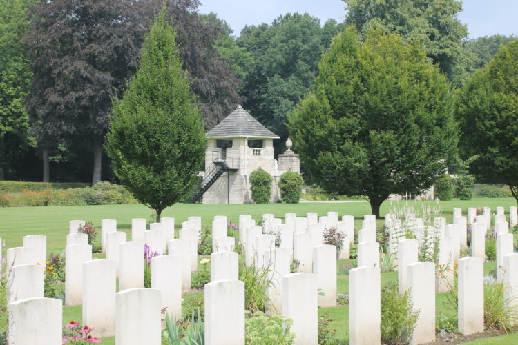 Weiße Grabmale auf dem Britischen Ehrenfriedhof auf einer grünen Wiese, Bäume im Hintergrund.