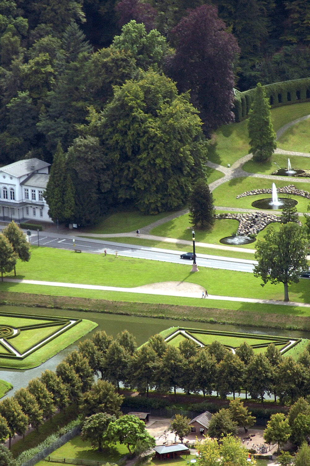 Luftaufnahme der symmetrisch gestalteten Klever Gartenanlage mit Hecken, einem Springbrunnen, einem kleinen Pavillon und von Bäumen umgebenen Wegen.