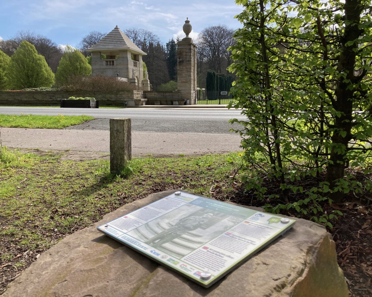 Hörstein mit Texttafel im Vordergrund, der Ehrenfriedhof im Hintergrund.