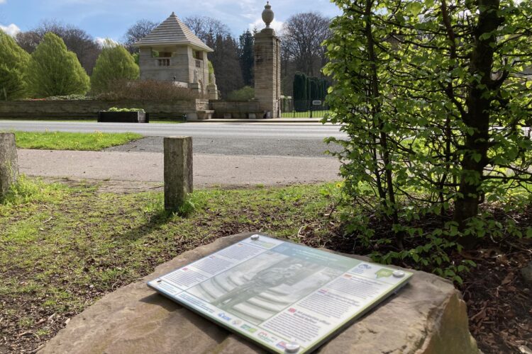 Hörstein mit Texttafel im Vordergrund, der Ehrenfriedhof im Hintergrund.