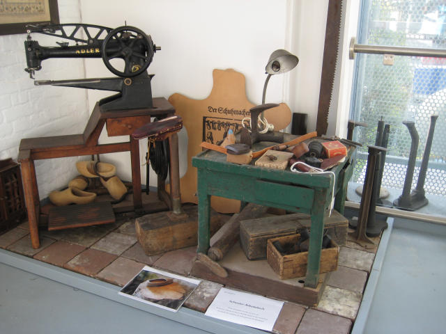 Alte Schuhmachermaschine auf Holztisch, grün lackierter Arbeitstisch mit Werkzeugen, Holzleisten und Schuhformen im Klever Schuhmuseum
