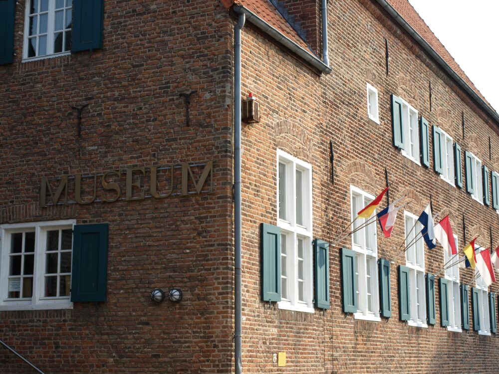 Backsteingebäude mit weißen Fensterläden und mehreren Flaggen an der Fassade, Schriftzug 'MUSEUM' an der Ecke sichtbar.