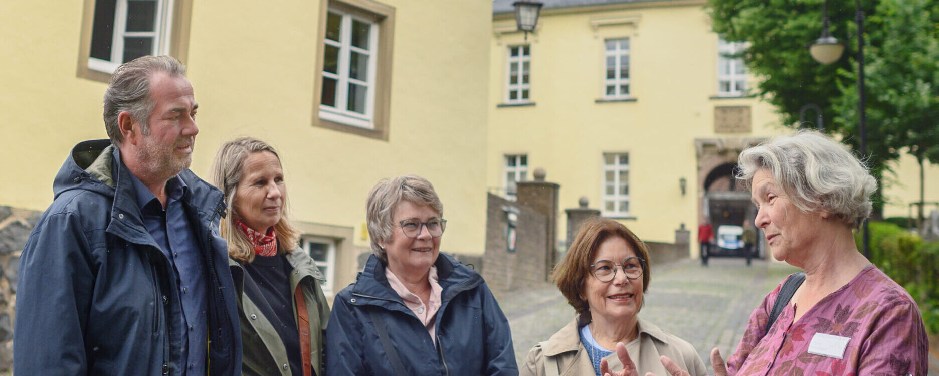 Gruppe von sechs Personen bei einer Führung an der Schwanenburg, eine Person erklärt etwas. Im Hintergrund ist der Turm der Schwanenburg sichtbar.