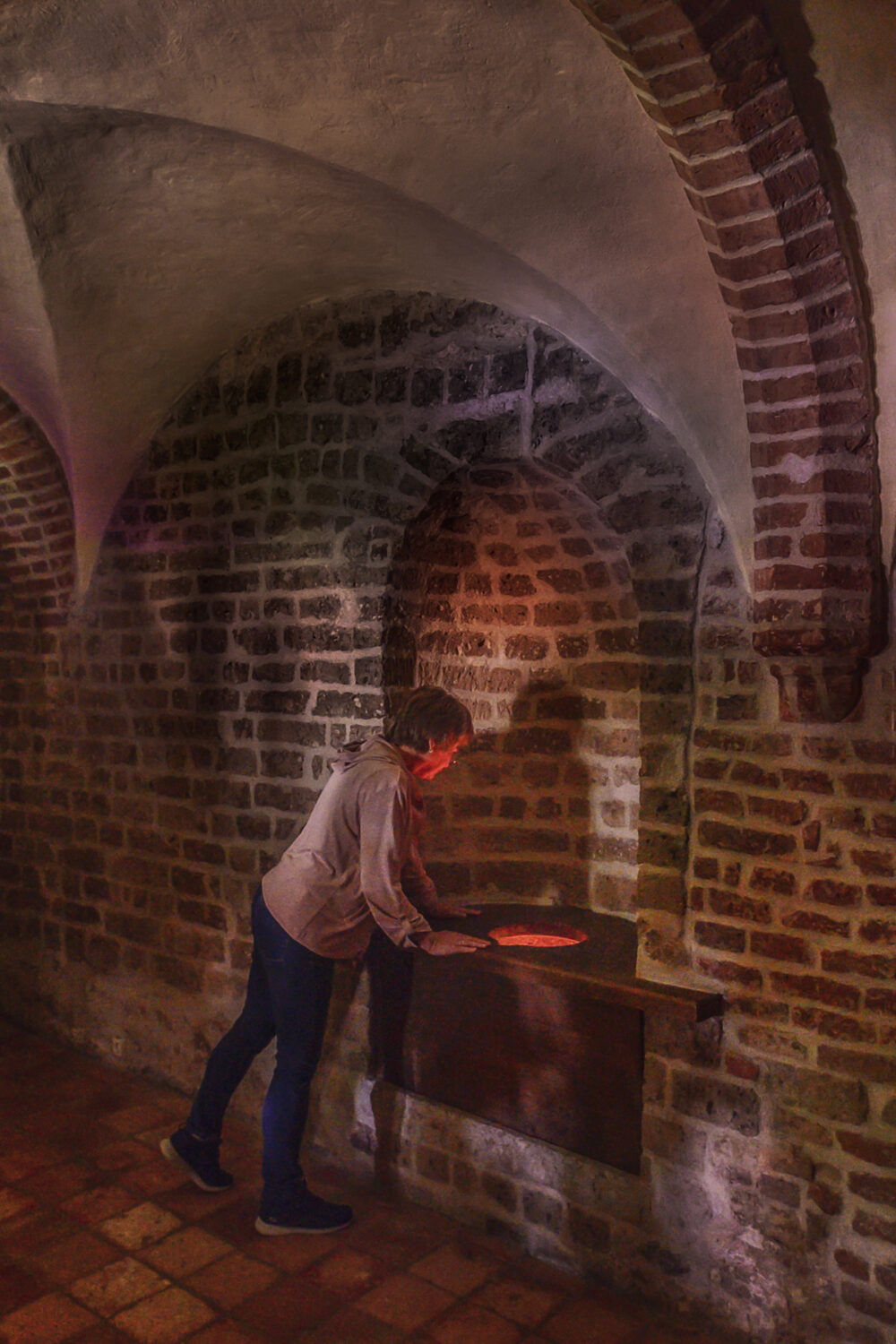 Ein Mann steht im Spiegelturm der Schwanenburg mit Ziegelwänden und gewölbten Decken.