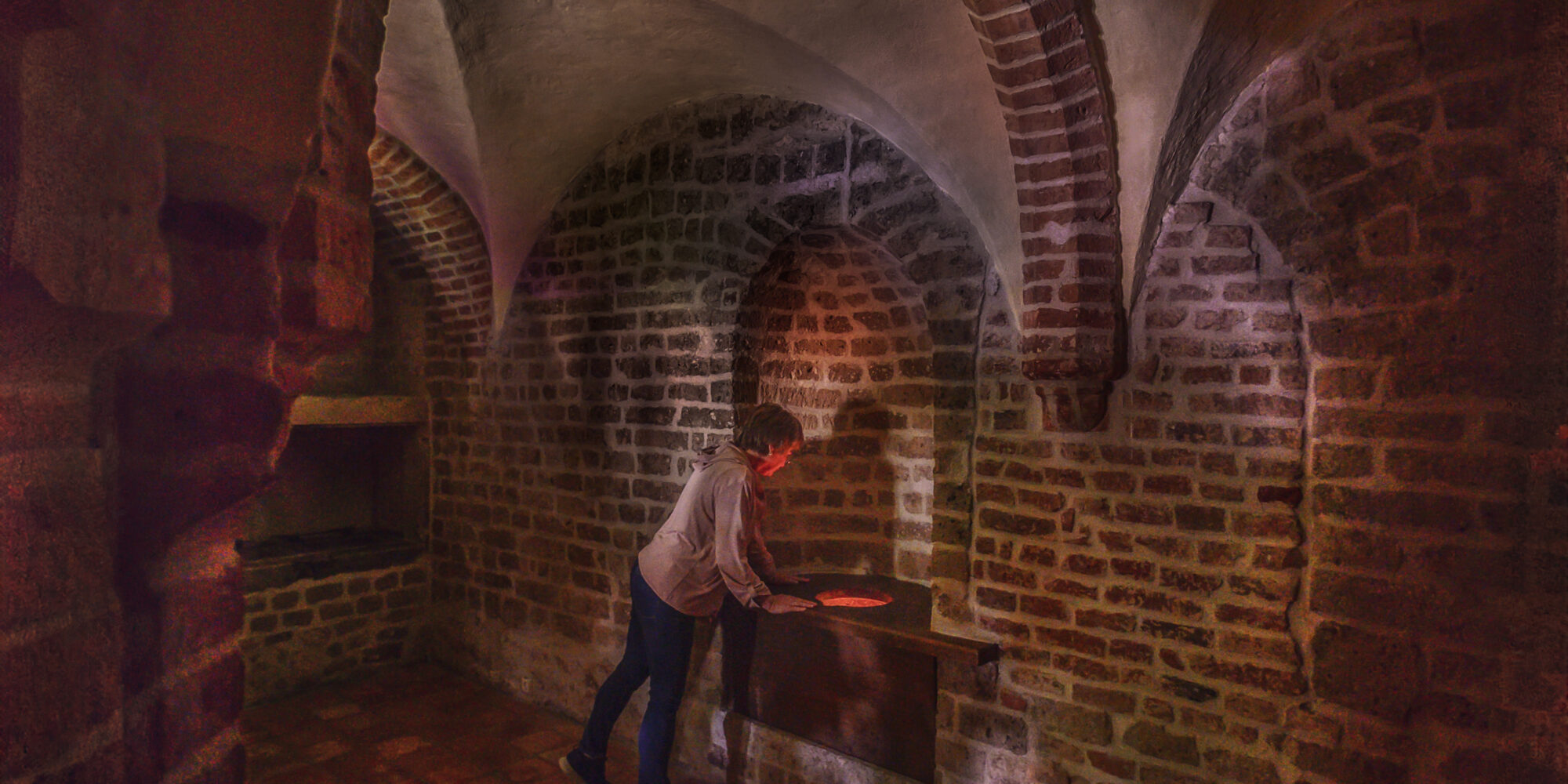 Ein Mann steht im Spiegelturm der Schwanenburg mit Ziegelwänden und gewölbten Decken.