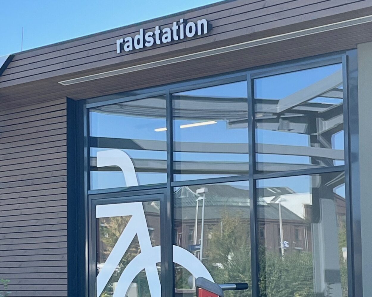 Das Gebäude mit der Aufschrift 'radstation' hat eine große Fahrrad-Silhouette an der Fensterfront. Vor dem Eingang steht eine rote Fahrradpumpe.