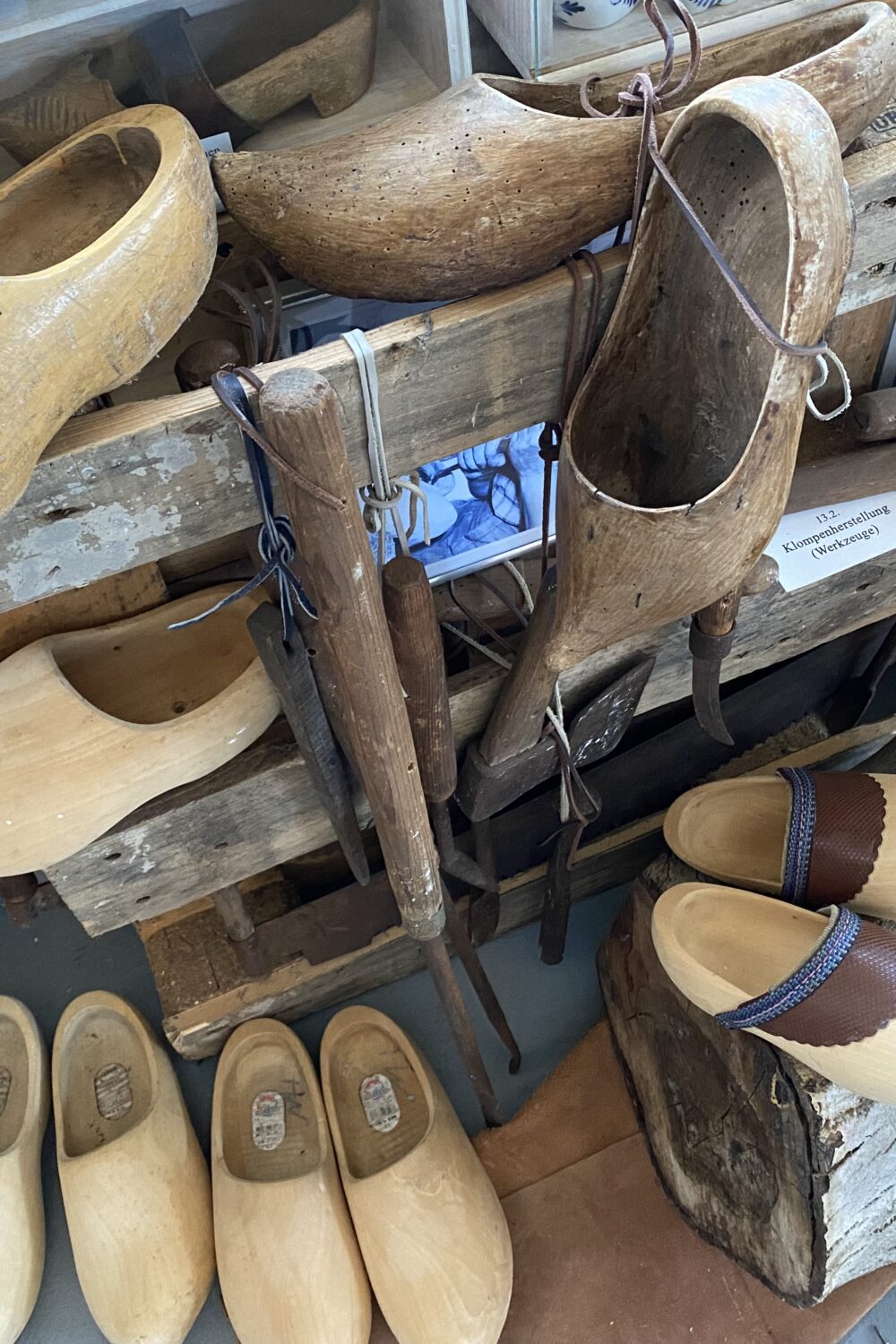 Verschiedene Holzschuhe im Klever Schuhmuseum, darunter bemalte und naturbelassene Modelle, einige hängen an einem Holzgestell, andere liegen auf Holzstücken.
