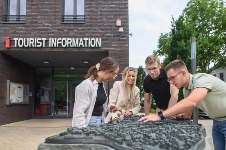 Gruppe vor Tourist-Information betrachtet taktiles Stadtmodell von Kleve auf einem Podest im Freien