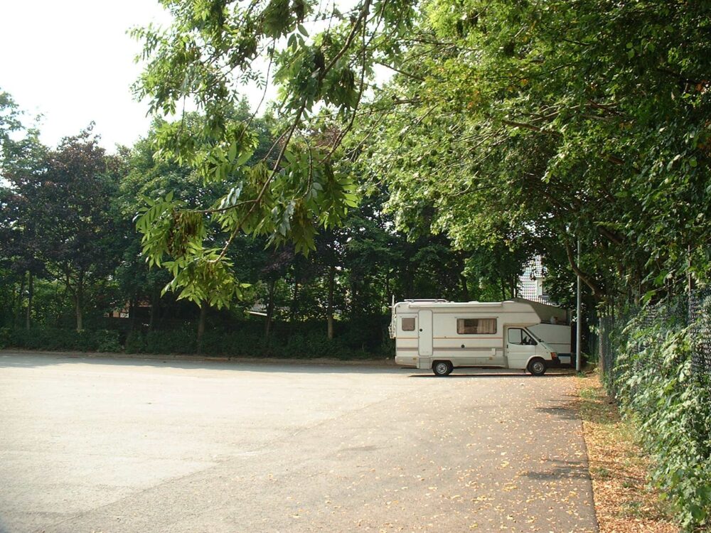 Weißes Wohnmobil auf einem Stellplatz, grüne Bäume drum herum