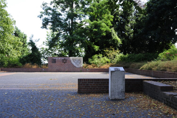 Gedenkstätte am Synagogenplatz mit einem Ziegelmauerstück, einer Davidstern-Skulptur und einer Wand mit Kerzenhaltern.