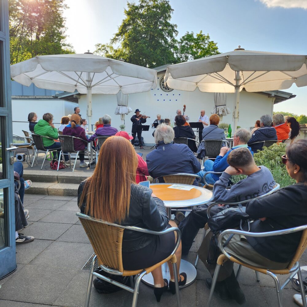 Dachterrasse des Cafe Moritz im Museum Kurhaus Kleve mit mehreren Personen an Tischen mit Sonnenschirmen