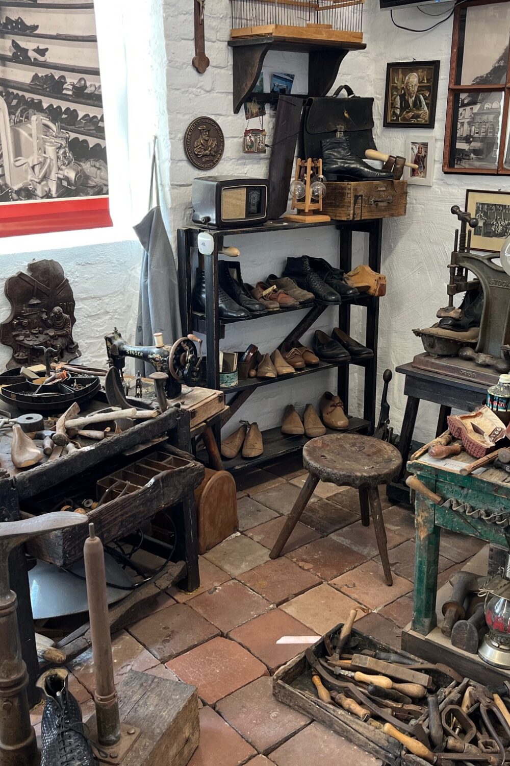 Werkstatt mit antiken Schuhmacherwerkzeugen, Lederschuhen, Holzstühlen und historischen Fotos an den Wänden im Klever Schuhmuseum