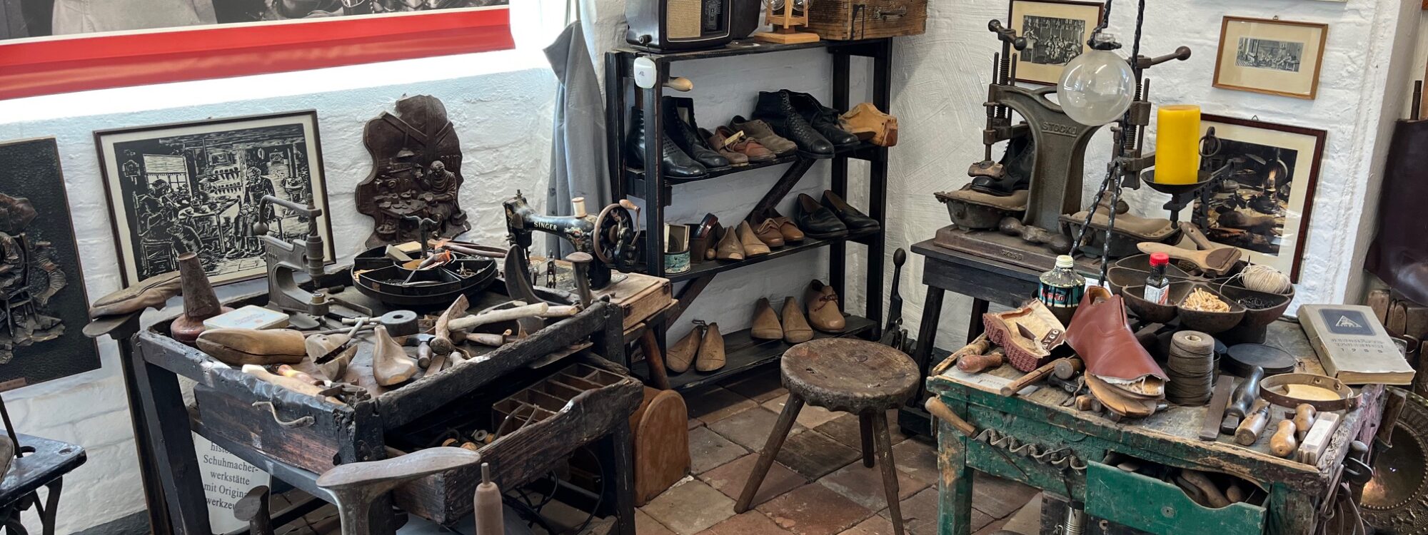 Werkstatt mit antiken Schuhmacherwerkzeugen, Lederschuhen, Holzstühlen und historischen Fotos an den Wänden im Klever Schuhmuseum