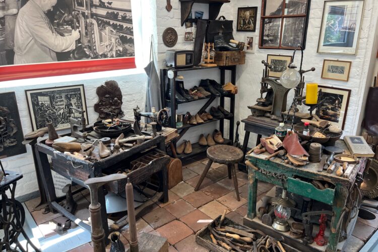 Werkstatt mit antiken Schuhmacherwerkzeugen, Lederschuhen, Holzstühlen und historischen Fotos an den Wänden im Klever Schuhmuseum