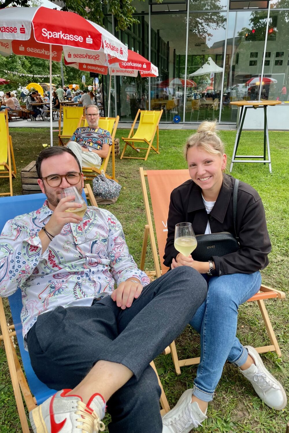 Ein Mann und eine Frau sitzen in gelben Liegestühlen und trinken Wein.