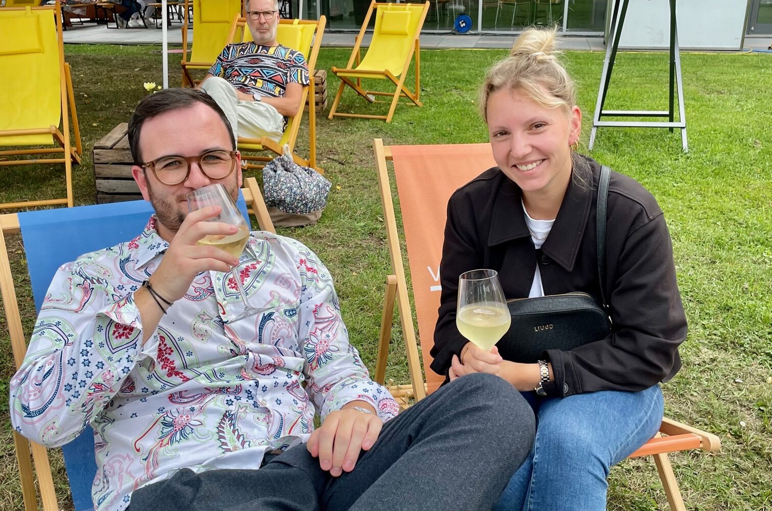 Ein Mann und eine Frau sitzen in gelben Liegestühlen und trinken Wein.