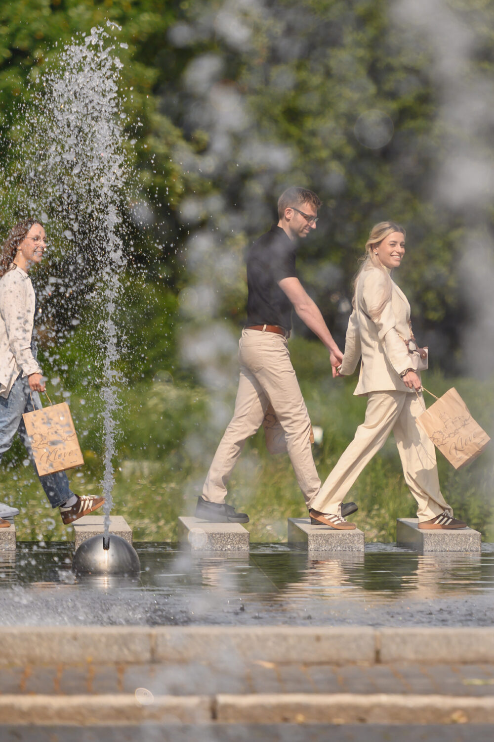 Gruppe von jungen Menschen läuft mit Tüten an einem Wasserspiel vorbei.