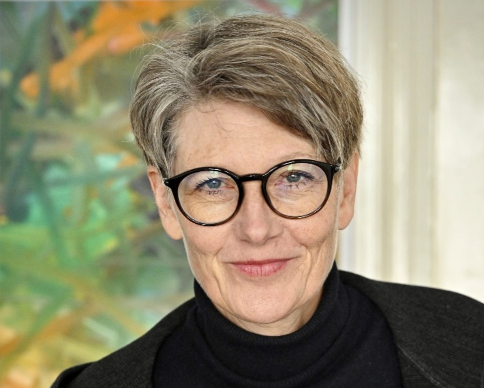 Foto der Privatdozentin Britta Behm vor einem grün-orangenem Hintergrund