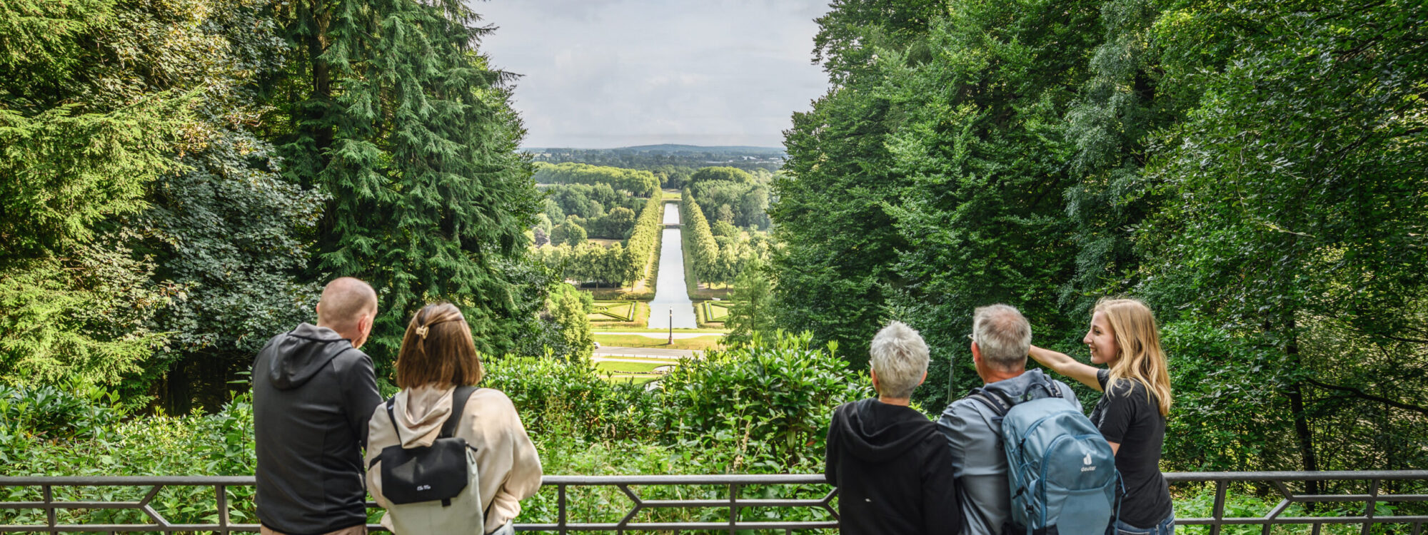 Fünf Personen an einem Zaun im Wald und schauen sich die schöne Aussicht auf einen Kanal an
