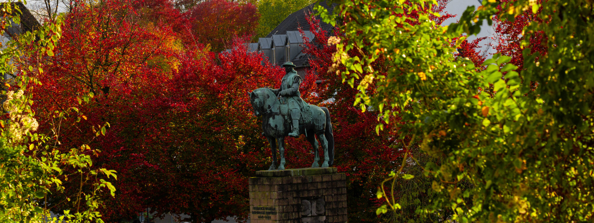 Skulptur mit einem Mann auf einem Pferd zwischen Bäumen mit roten ud gelben Blättern.