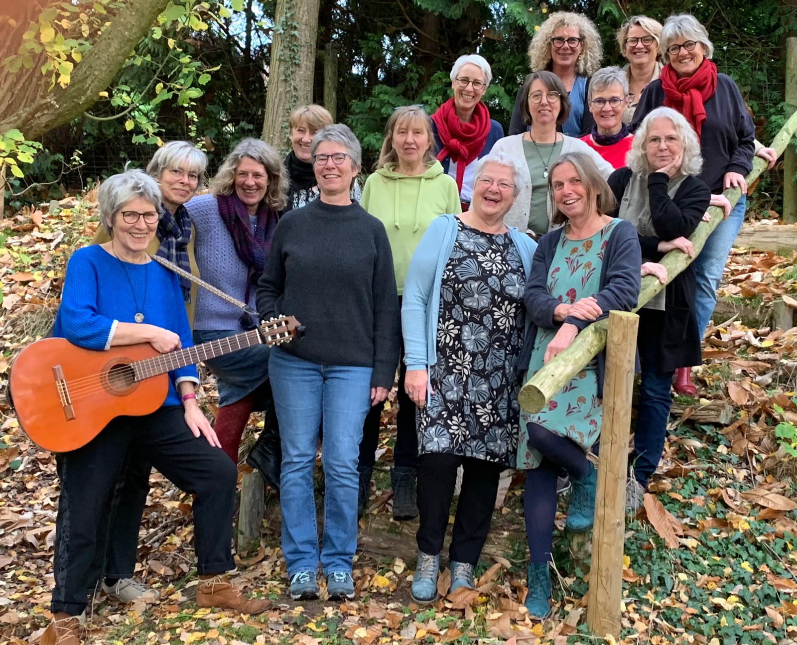 Gruppe von Frauen unterschiedlichen Alters. Alle gehören zum Chor ByHeart. Sie stehen im herbstlichen Wald auf einer Treppe. Eine Frau hält eine Gitarre.